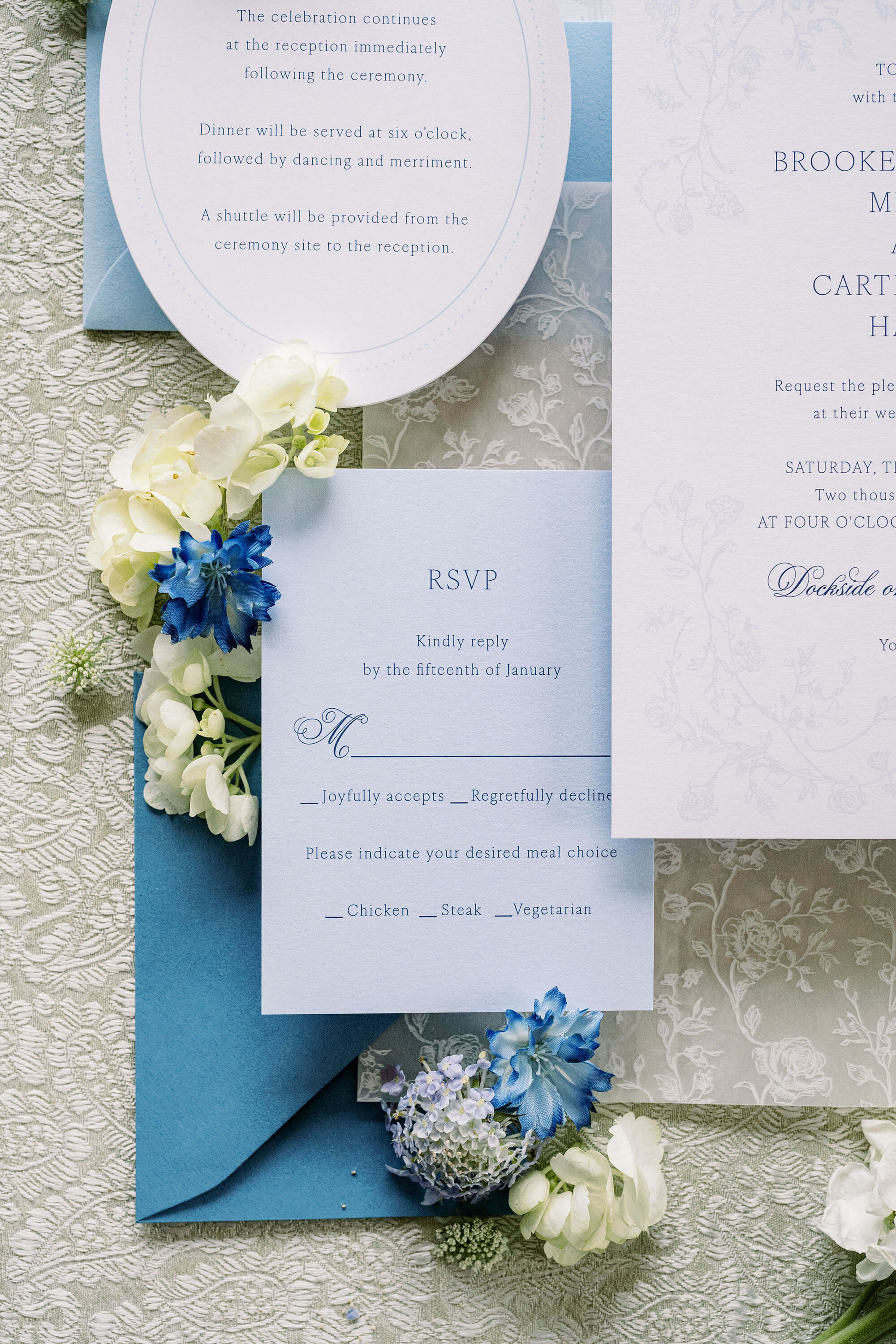 Wedding invitation set with RSVP card, blue envelope, and floral decorations on a textured surface.