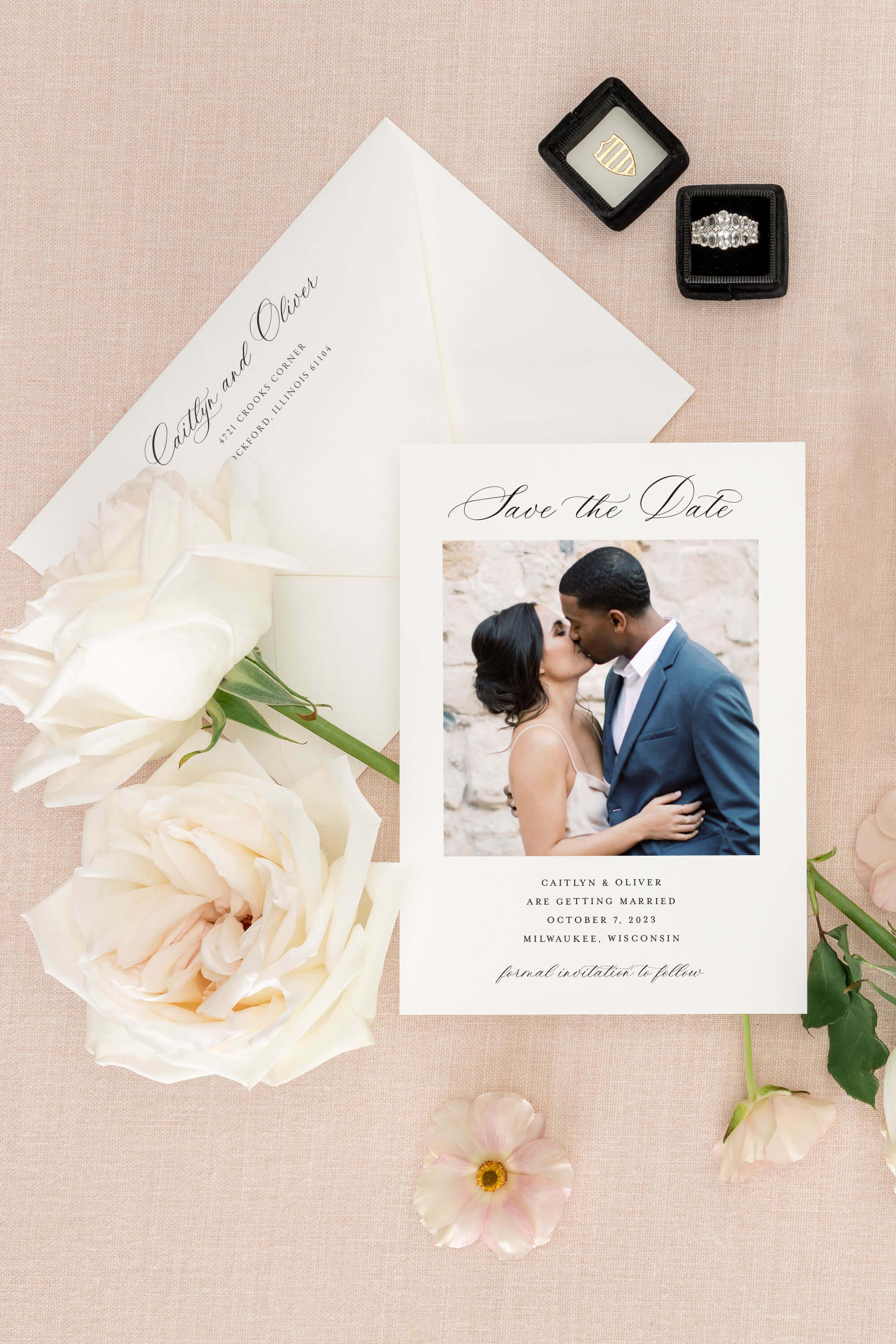 Wedding  'Save the Date' card, flowers, and rings on a beige background