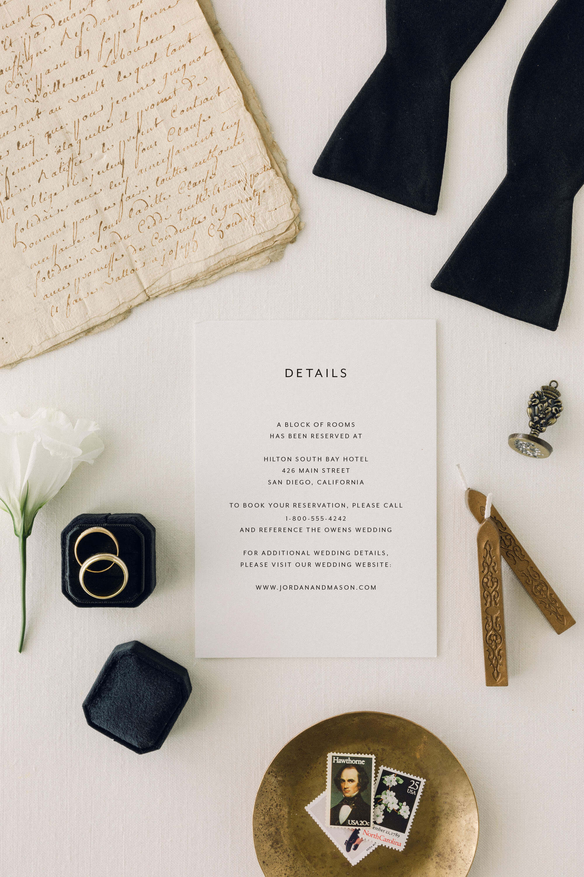 Simple Wedding invitation detail card with rings, flowers, and other wedding accessories on a white surface