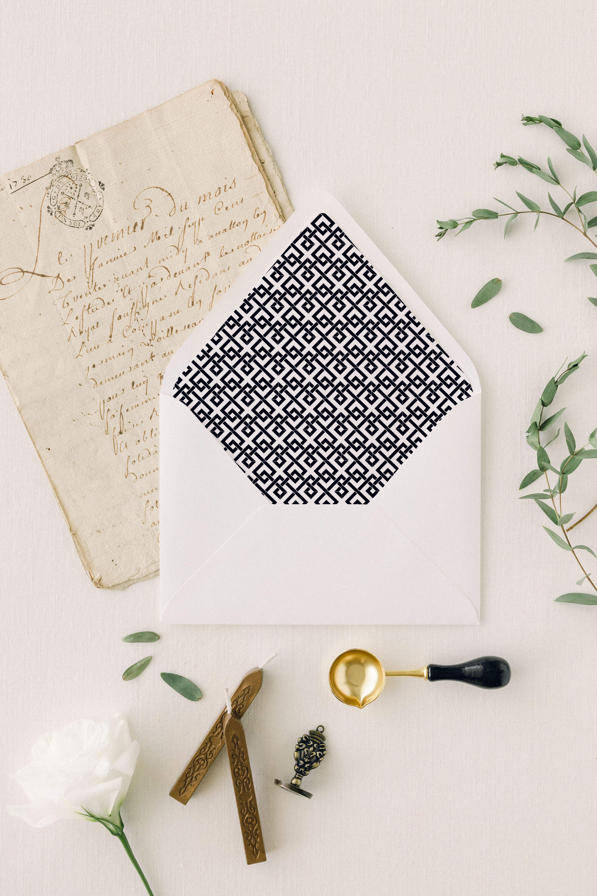 Simple, geometric Patterned wedding invitation envelope liner, gold pen, and greenery on a light background