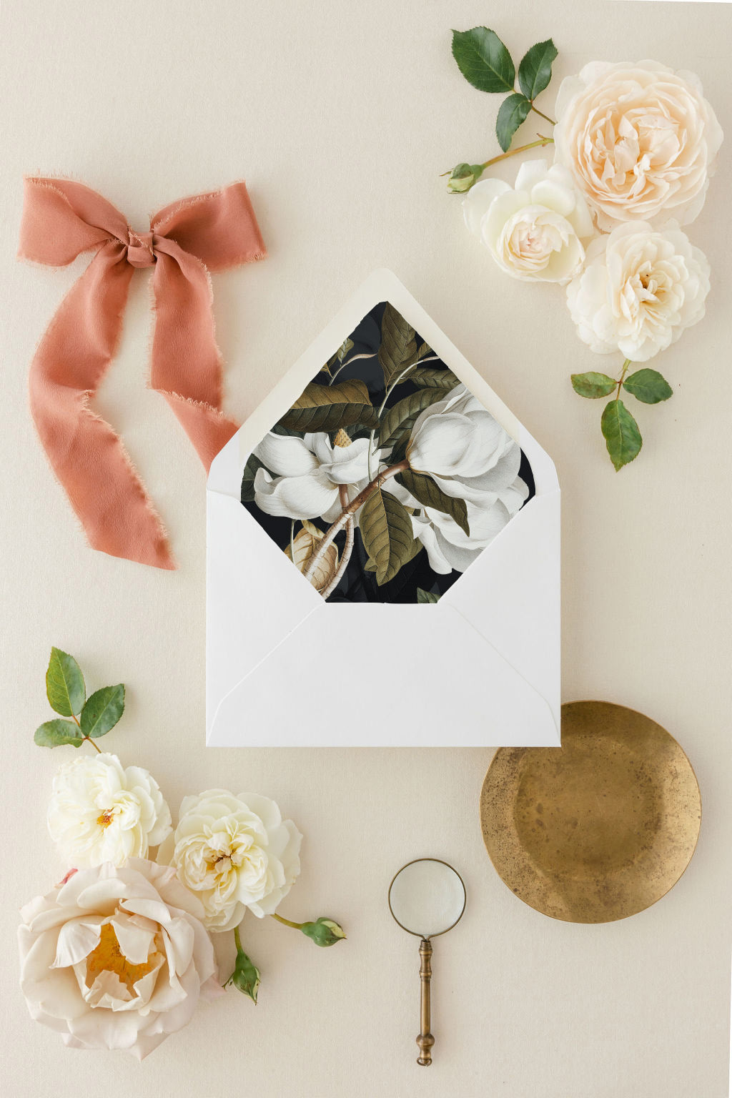 Open white envelope with modern floral envelope liner design, surrounded by flowers and a pink bow on a light background